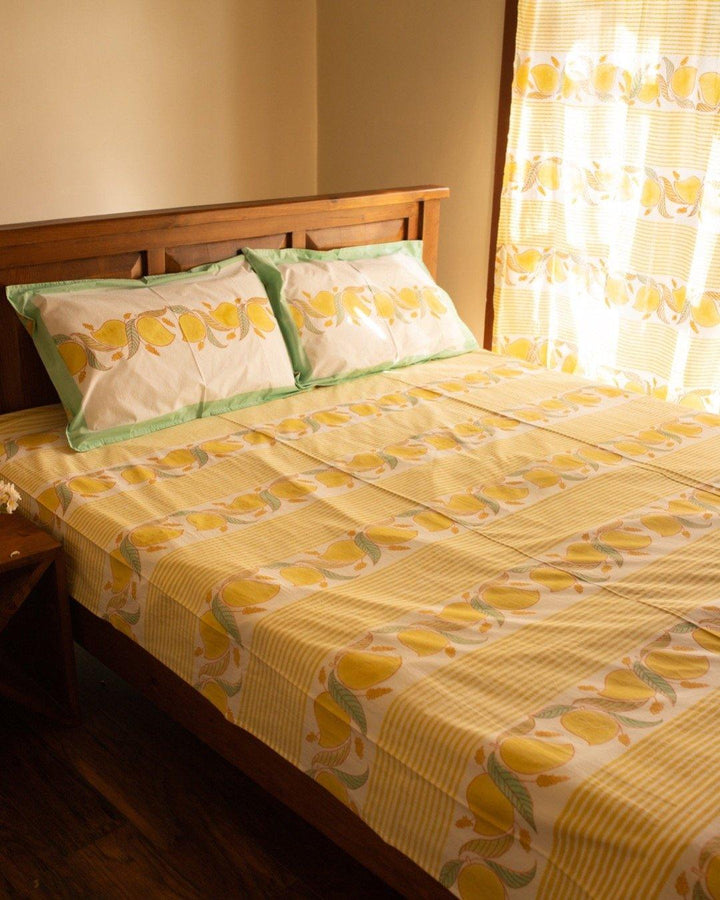Bedroom set up with yellow block printed Jaipuri bedsheets with mango and vine themed patterns on them, while sunlight streams through the curtains