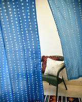 Blue ombre bandhani tie dye curtains with a chair and mirrorwork cushions in the background