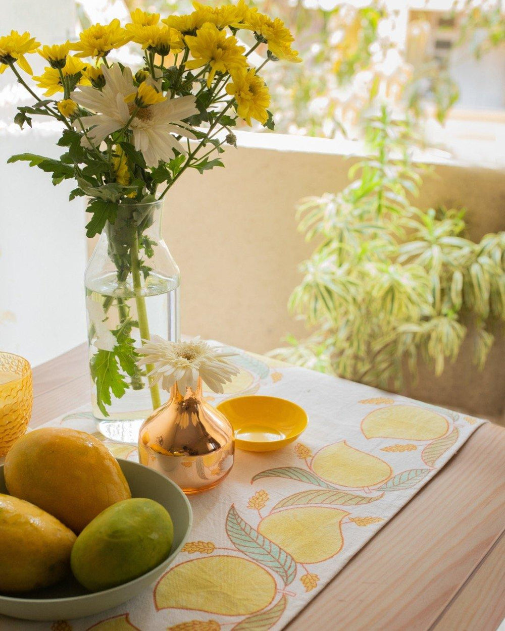 Table setting with block printed mango themed cotton table runner, a glass vase with flowers and a bowl full of mangoes